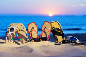 flip flops sticking out of sand with sunset on horizon